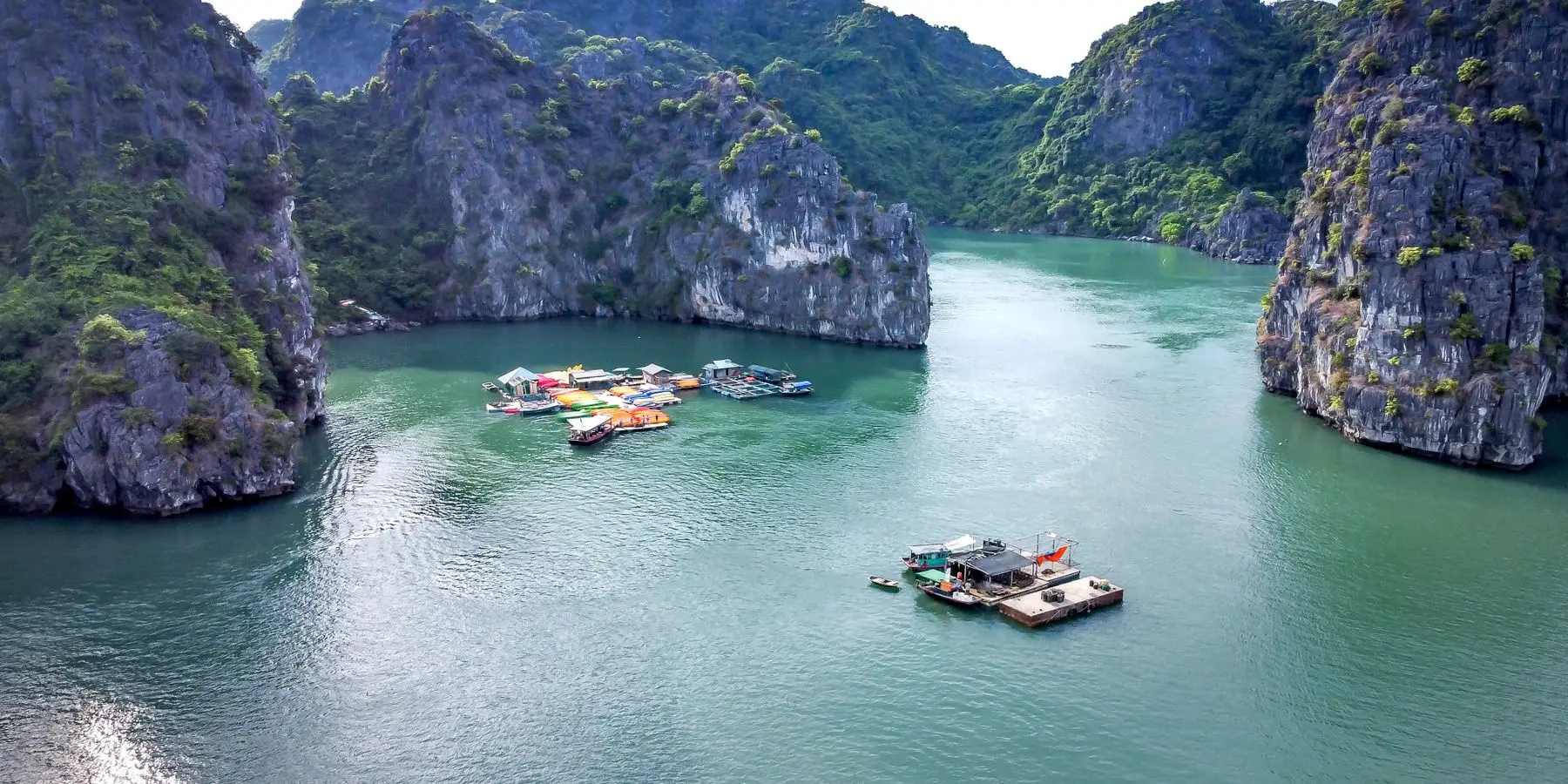 Limestone karsts rising from the water in Ha Long Bay, with small boats and a floating village below.